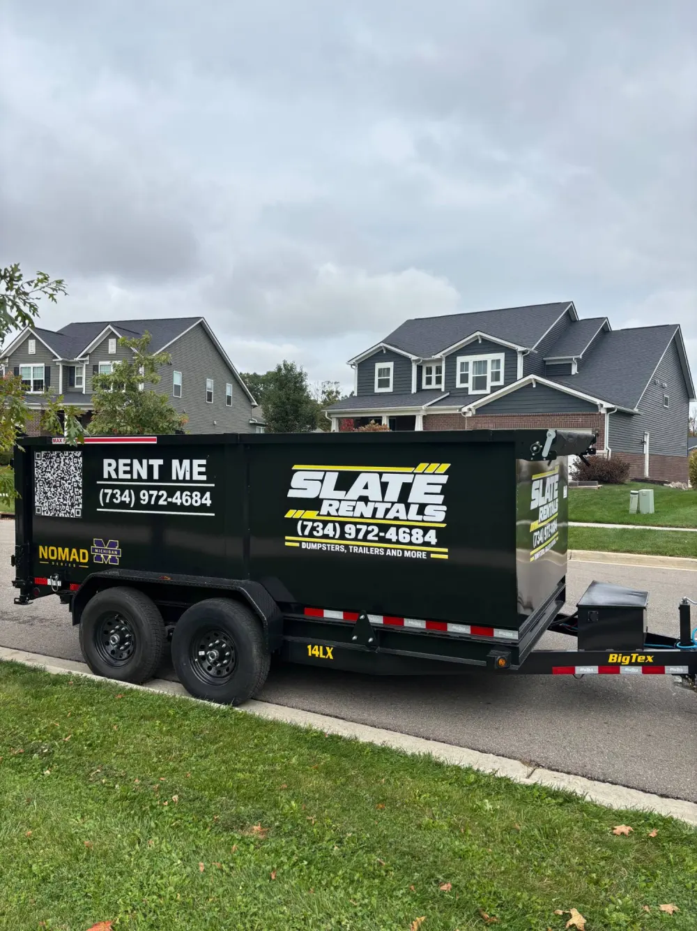Dump trailer parked at the curb in front of two-story homes in a newer subdivision.